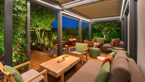 An outdoor patio area with wooden furniture, a cushioned sofa, and a dining table. - Hotel Metropolitan (Bologna)