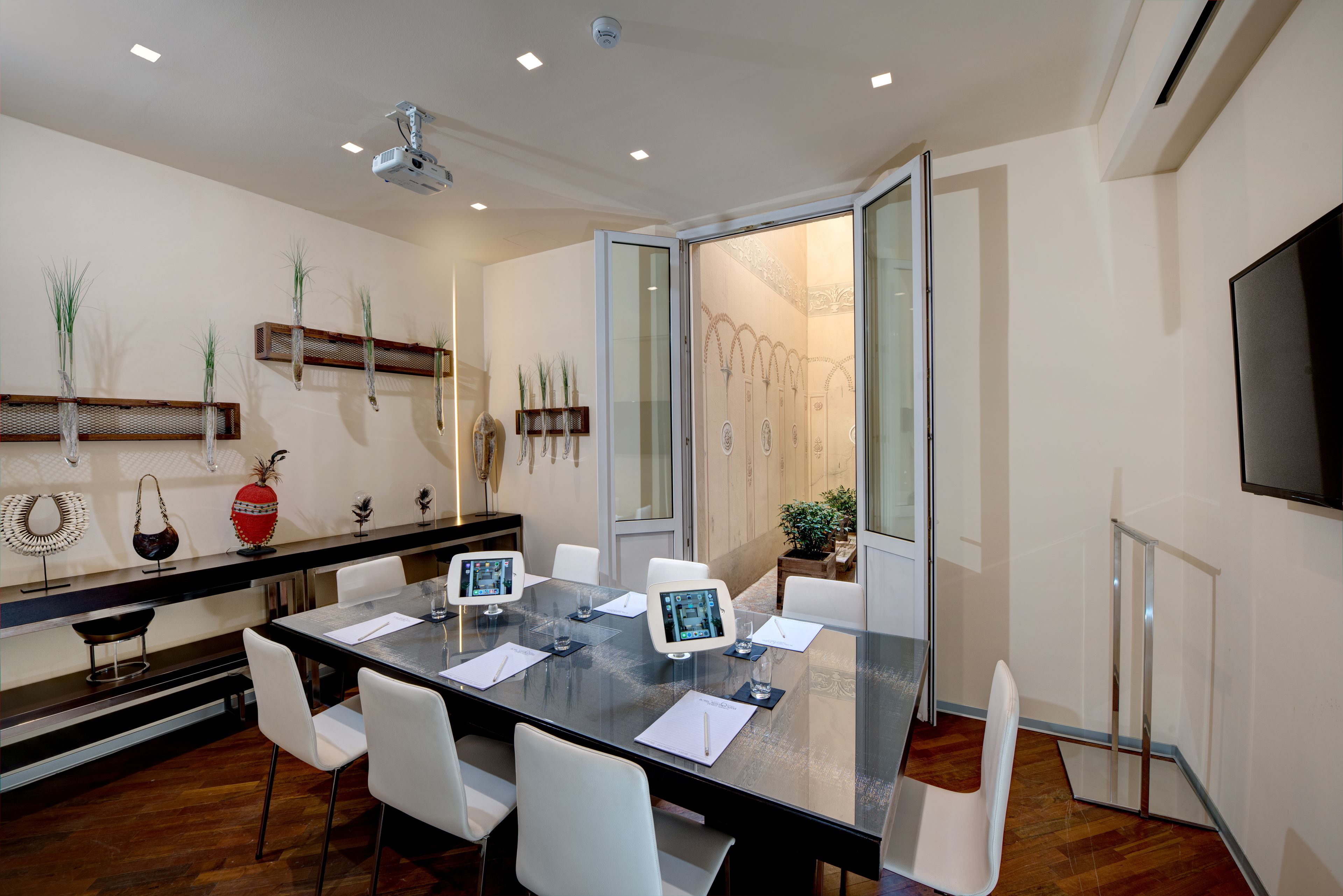 Un salón de conferencias con una mesa de vidrio, sillas blancas y una pantalla grande.