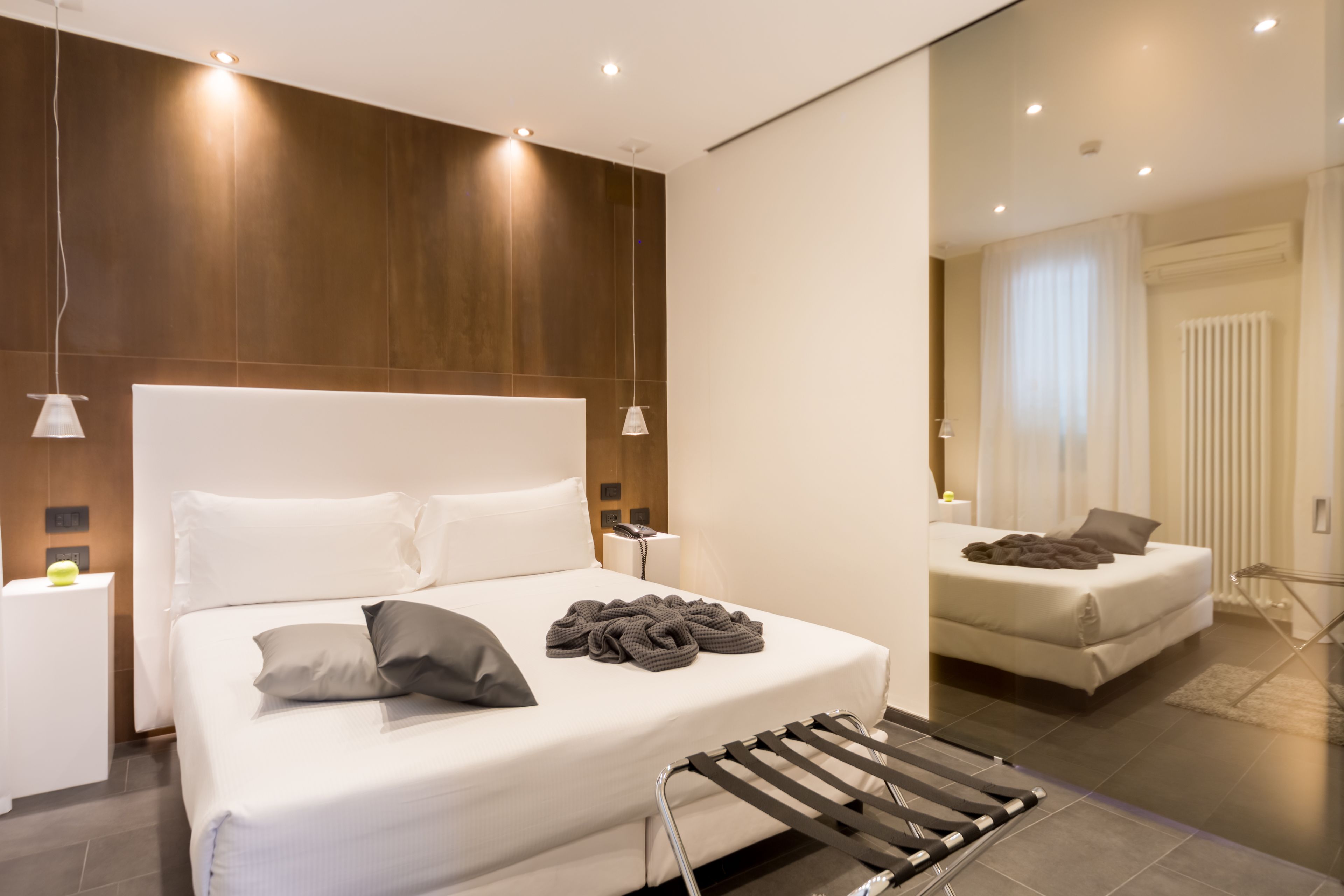 Een moderne hotelkamer met een groot bed, nachtkastje, spiegel en hanglamp.