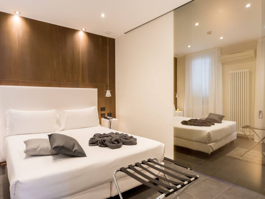 Een moderne hotelkamer met een groot bed, nachtkastje, spiegel en hanglamp.