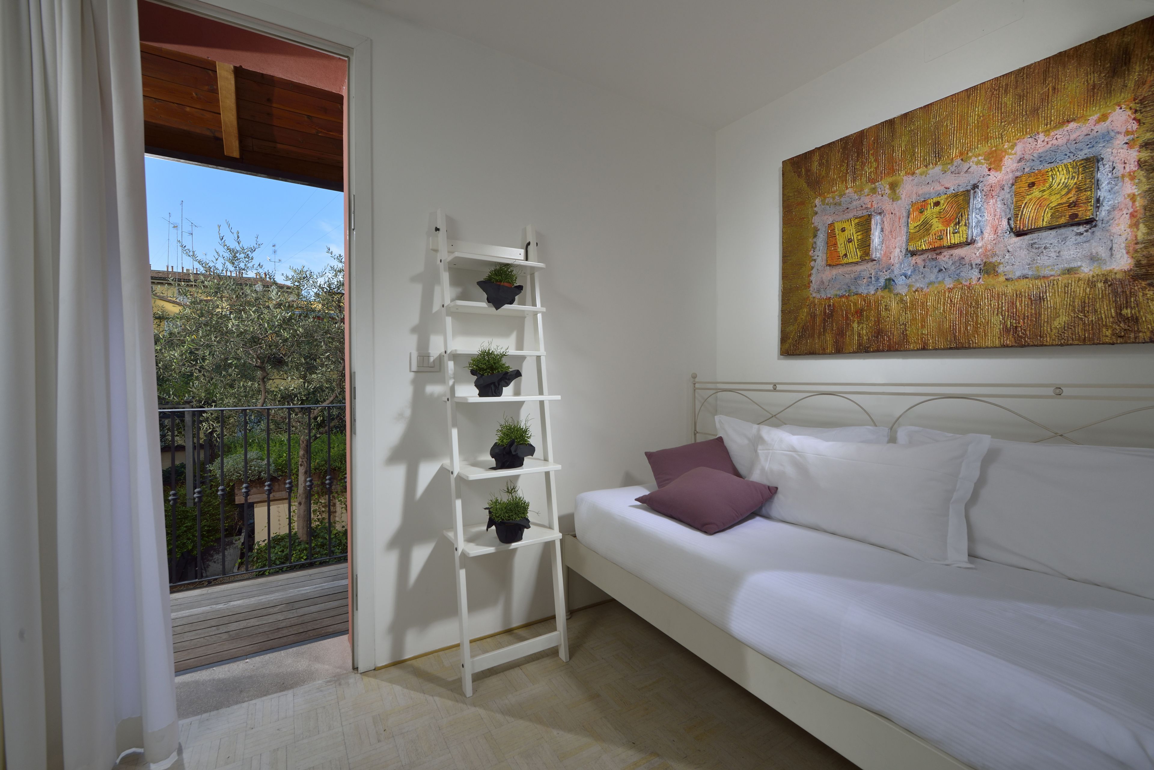 Ein Schlafzimmer mit einem weißen Bett, einer weißen Leiter mit Topfpflanzen, einem Balkon mit Geländer und einem großen, abstrakten Gemälde an der Wand.