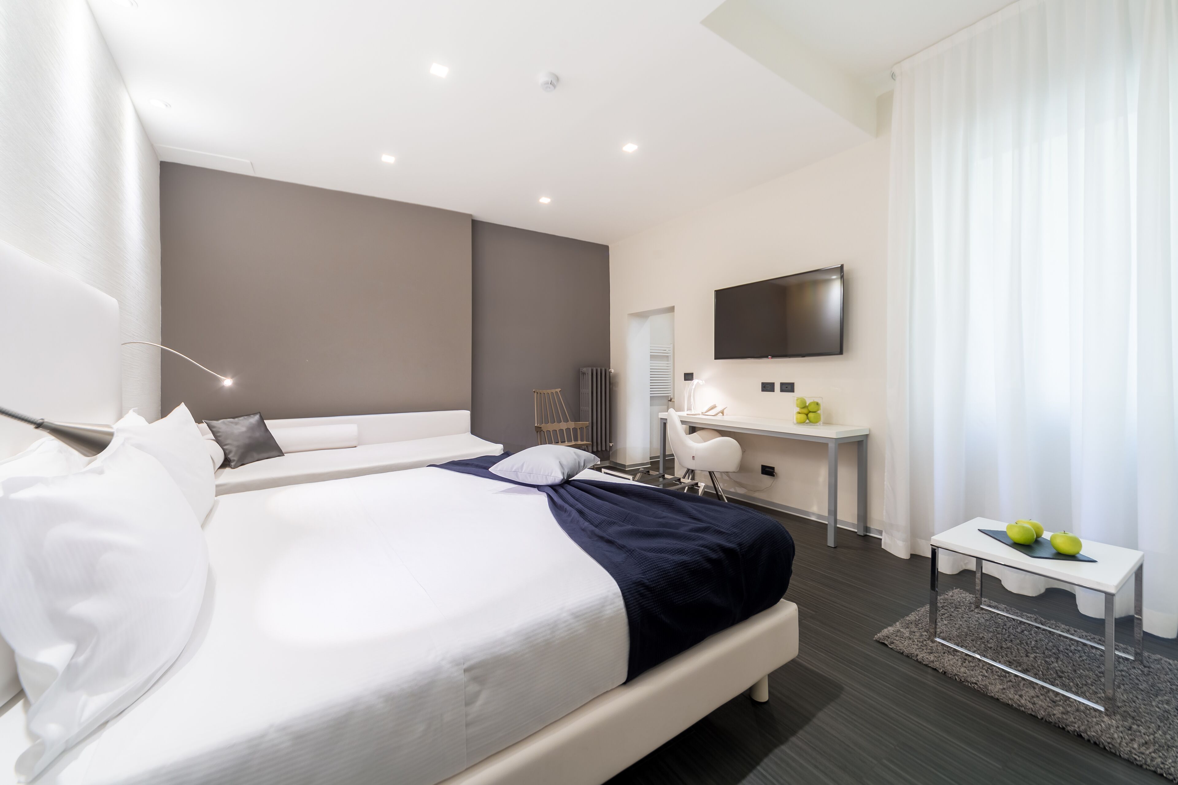 Een moderne hotelkamer met een groot bed, een bureau, een flatscreen televisie en een klein tafeltje met appels.