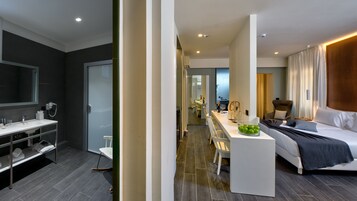 Habitación de hotel moderna con una cama grande, baño independiente, zona de comedor y vistas a la ciudad.