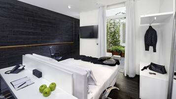 Camera da letto moderna con una parete d'accento in legno scuro, un letto bianco, una scrivania con un telefono, un quaderno e delle mele, e vista su del verde all'esterno.
