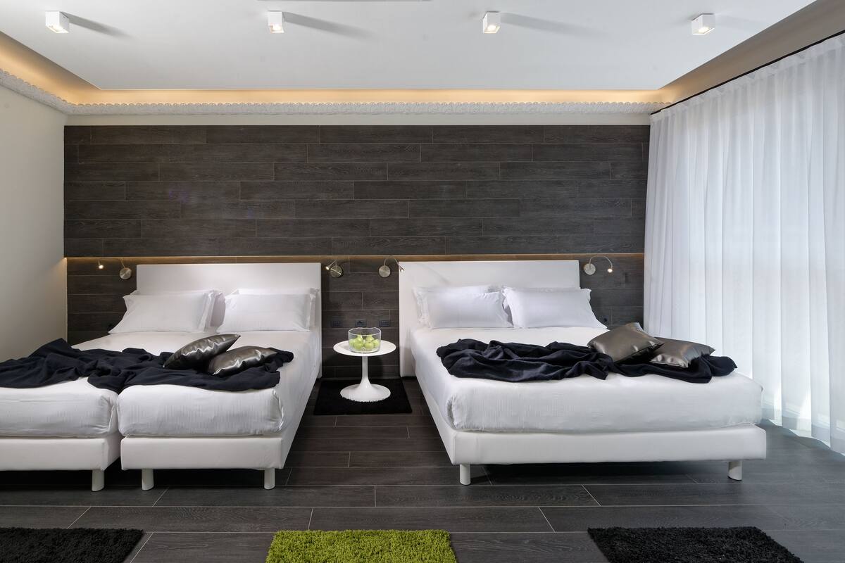 Ein modernes Hotelzimmer mit zwei Betten, einem kleinen runden Tisch und einem großen Fenster mit Vorhängen.