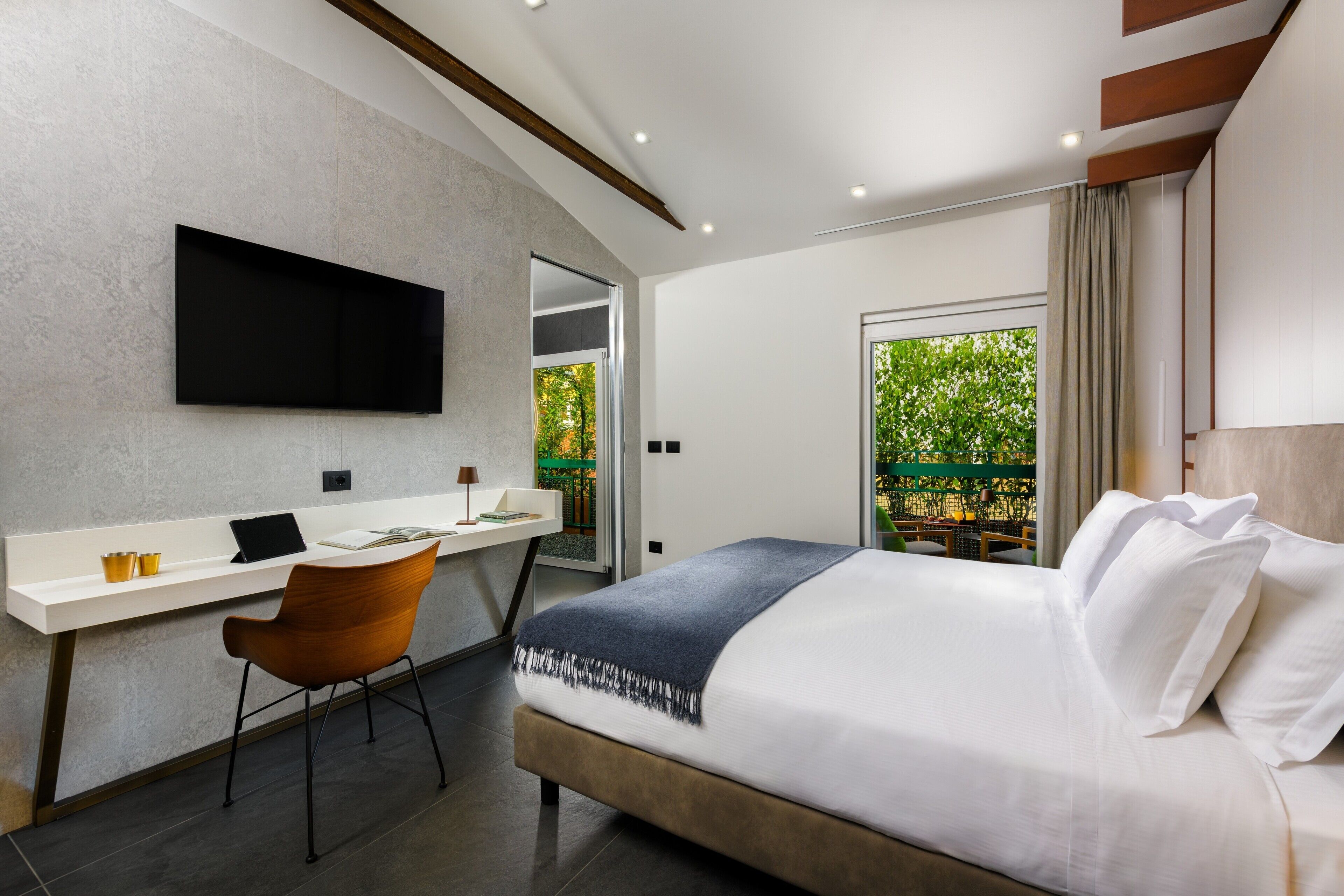 Habitación de hotel moderna con una cama grande, un escritorio con silla, un televisor de pantalla plana en la pared y vista a zonas verdes.