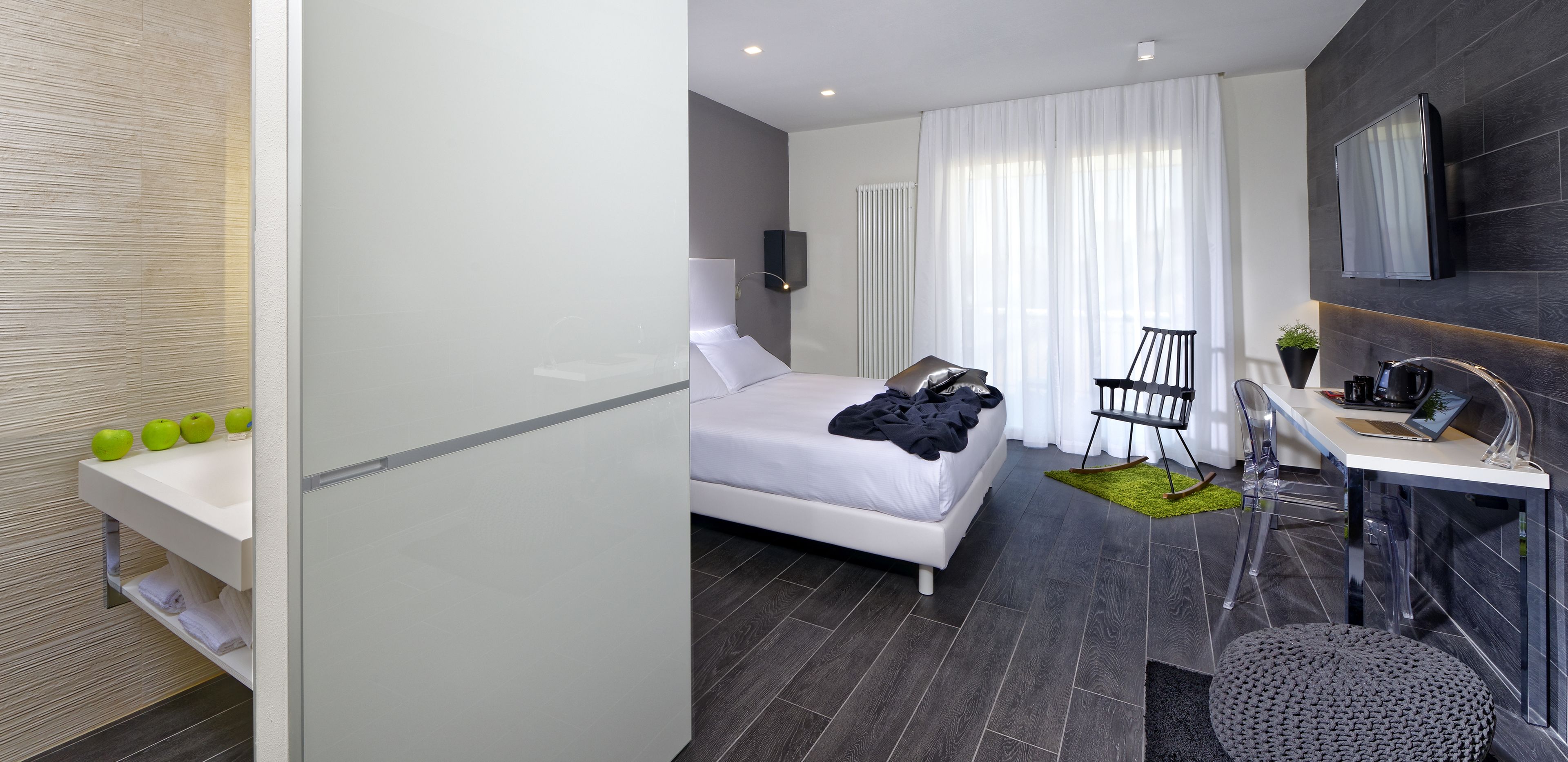 A modern hotel room with a bed, a desk, a chair, a TV, and a bathroom area.
