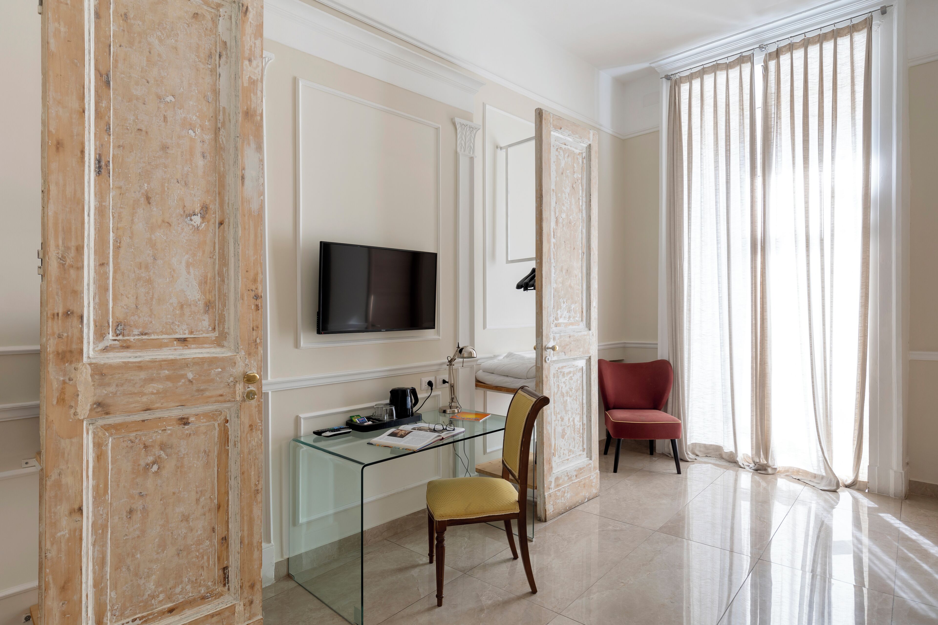 A room with a glass desk, a television, a chair, and a red chair.