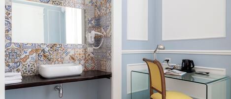 A bathroom with a tiled backsplash, a white sink, a mirror, a glass shower enclosure, and a wooden chair.