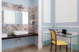 A bathroom with a tiled backsplash, a white sink, a mirror, a glass shower enclosure, and a wooden chair.