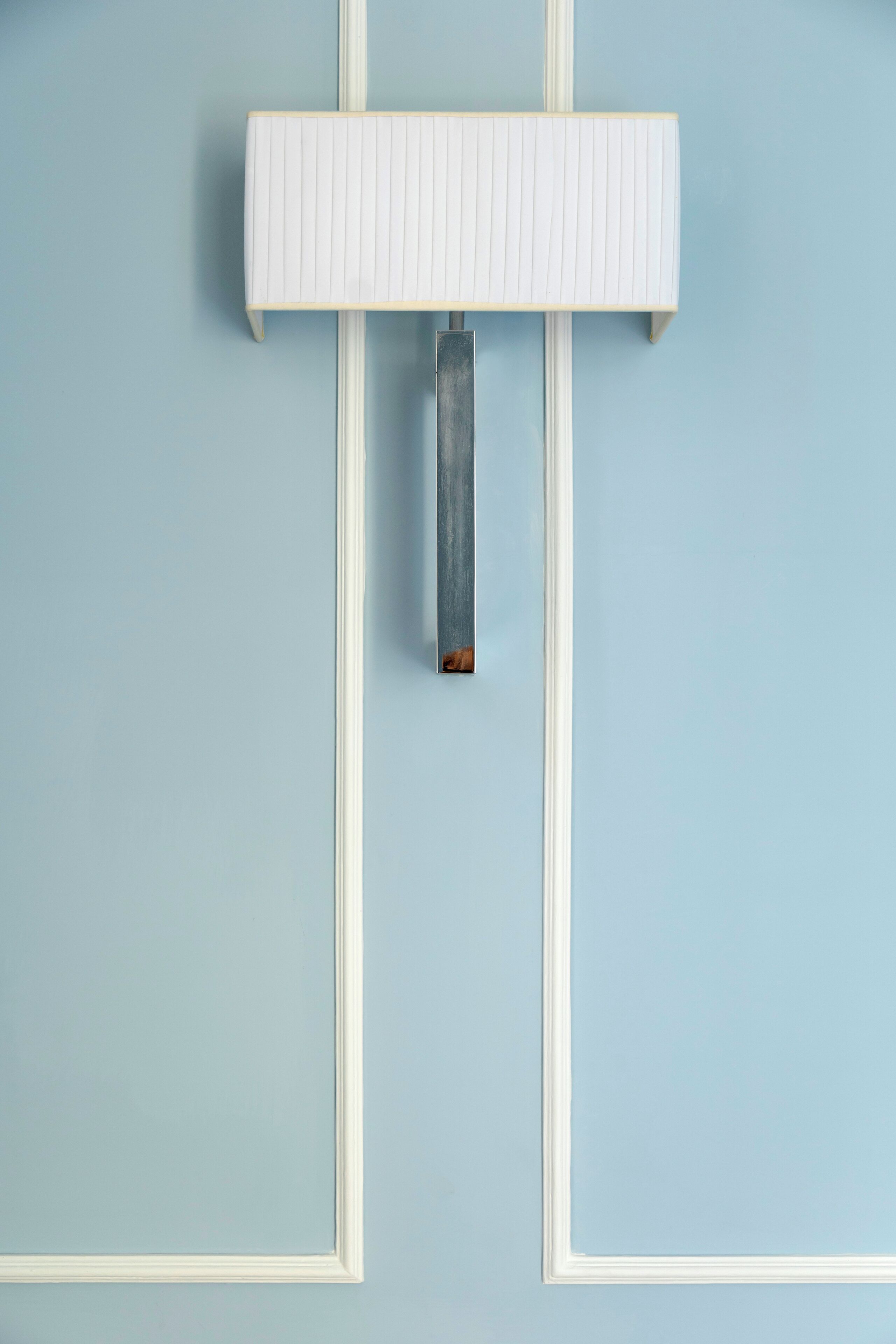 Um objeto retangular branco fixado na parede, com uma alça vertical, montado em uma parede azul claro.