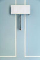Objeto rectangular blanco, fijado a la pared con una asa vertical, sobre un fondo azul claro.