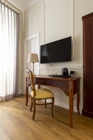 A hotel room with a wooden desk, a chair, a television, and a wardrobe.