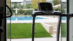 A home gym with a treadmill and a stationary bike, overlooking a swimming pool and a lawn. - Hotel Victoria (Vicenza)