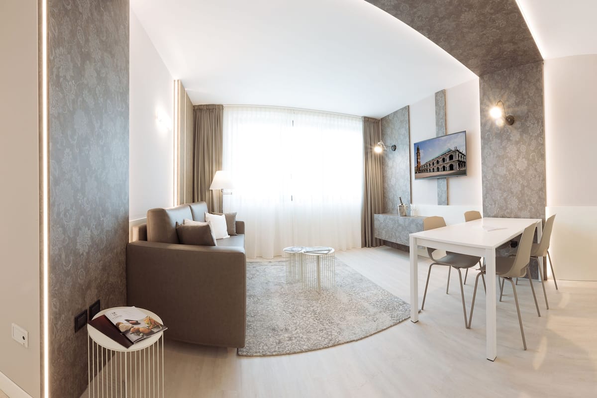 A modern hotel room with a living area, dining space, and a view of the cityscape.