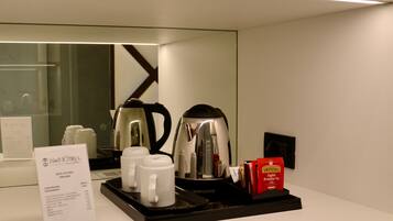 A hotel minibar setup with a coffee maker, two mugs, a kettle, and a tray with tea packets.