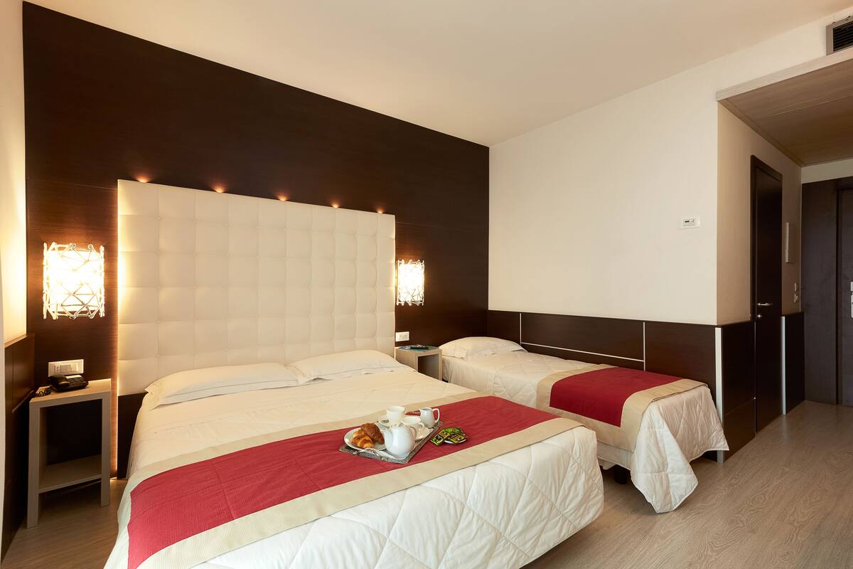 A hotel room with two beds, a bedside table with a lamp, and a tray with breakfast items.