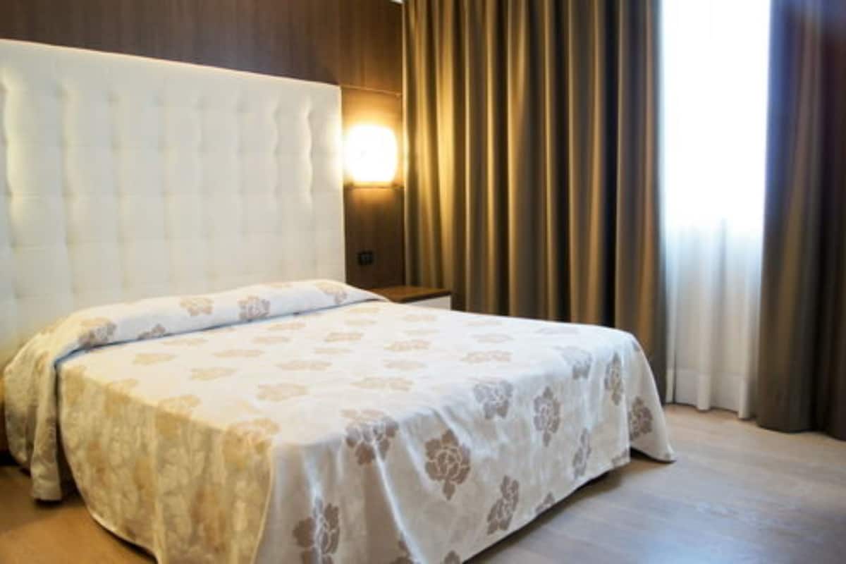 A hotel room with a large bed, a headboard, a wall-mounted light, and curtains.
