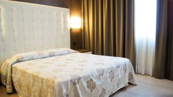 Ein Hotelzimmer mit einem großen Bett, einem Kopfteil, einer Wandleuchte und Vorhängen.