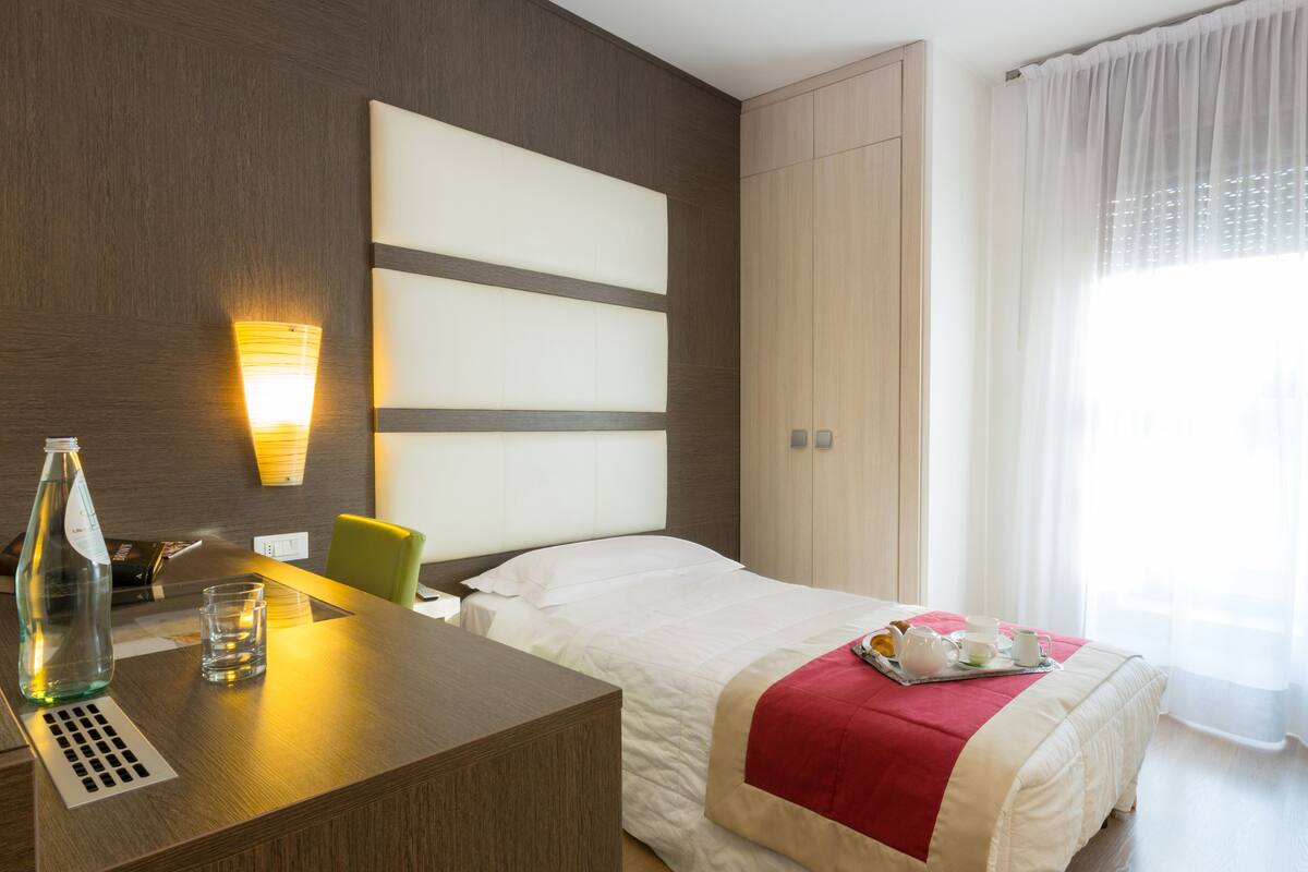 A hotel room with a bed, bedside table, lamp, and a window with curtains.