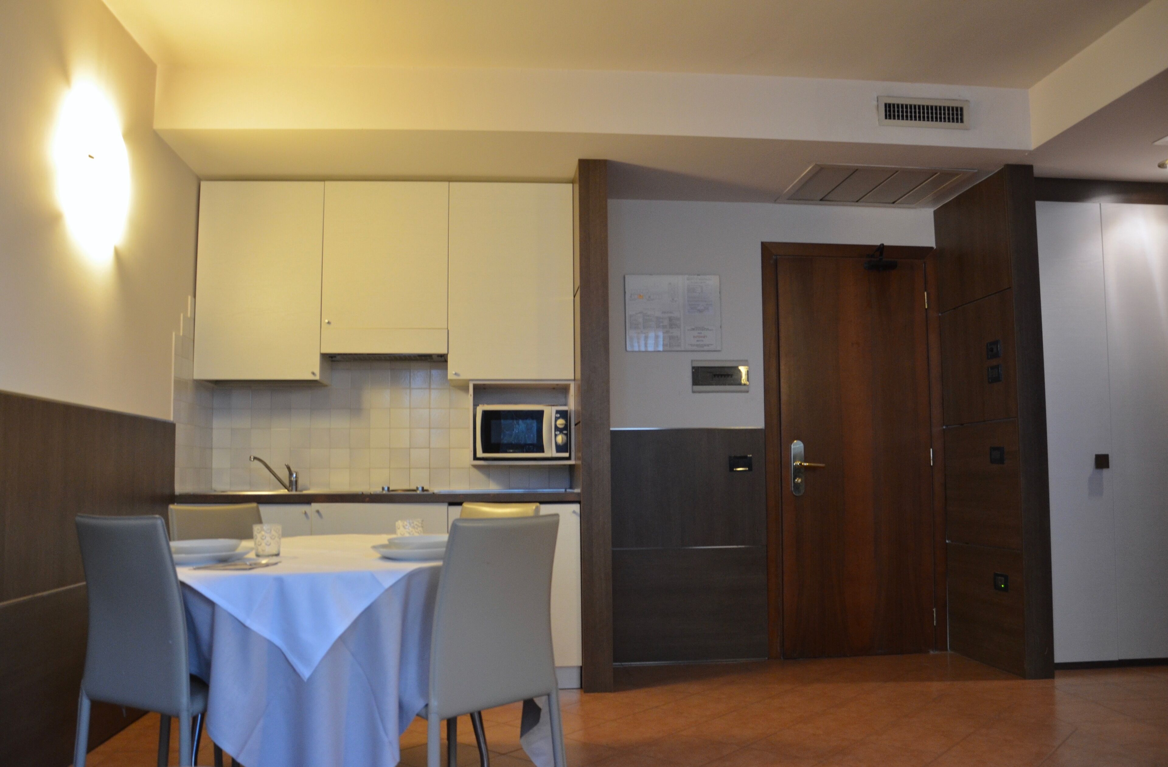 Cocina compacta con armarios blancos, microondas y zona de comedor con mesa y sillas.