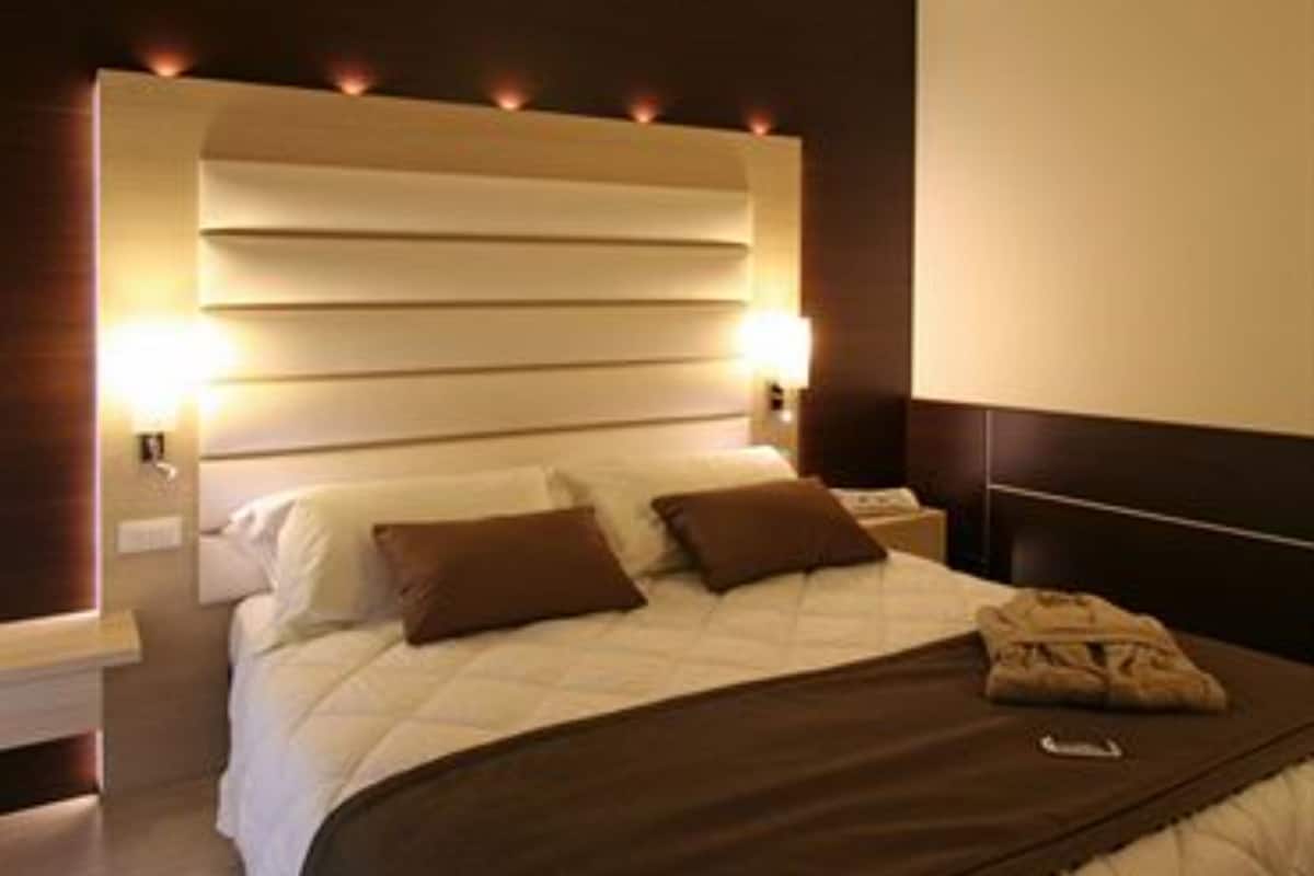 A modern hotel room with a large bed, a wooden headboard, and bedside lamps.