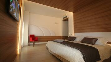 A modern bedroom with a large bed, a red chair, and a television mounted on the wall.