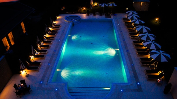 A swimming pool with a fountain, surrounded by lounge chairs and umbrellas, and a covered seating area with tables. - Hotel Victoria (Vicenza)