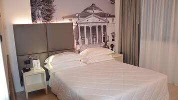 Una camera d'albergo con un letto grande, un comodino con una lampada e un affresco raffigurante un edificio classico.