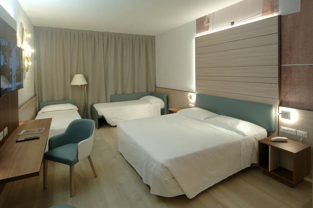 A hotel room with two single beds, a desk with a chair, a lamp, and a bedside table with a phone.