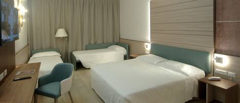 Habitación de hotel con dos camas individuales, un escritorio con silla, una lámpara y una mesita de noche con teléfono.
