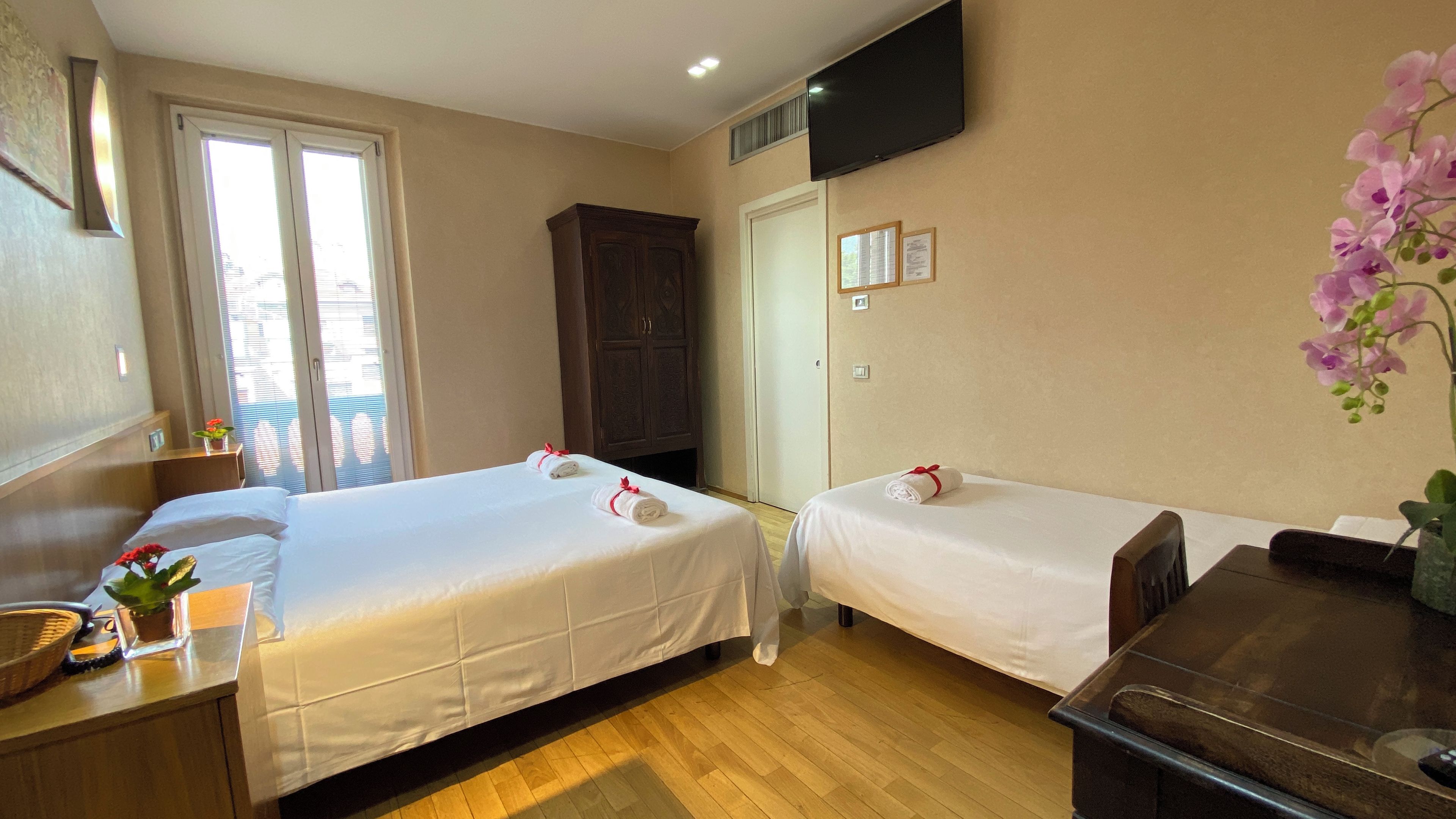 A hotel room with two beds, a desk, a TV, and a window with blinds.