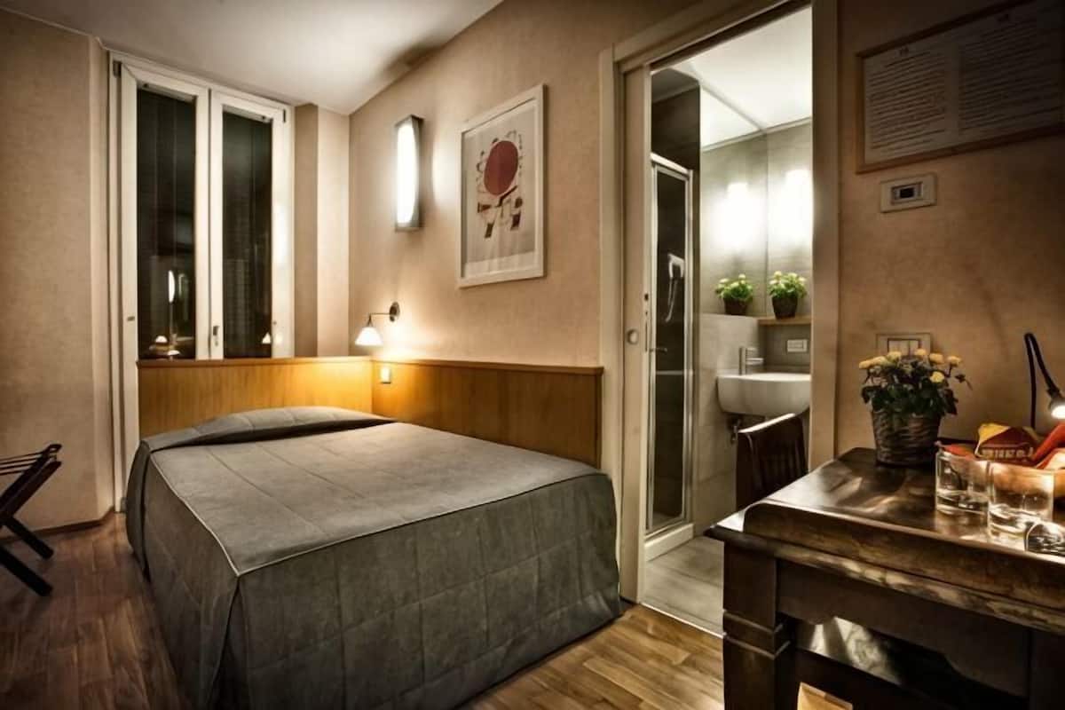 A bedroom with a bed, bedside table, lamp, and a door leading to a bathroom.