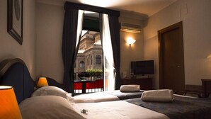 Habitación de hotel con dos camas, televisión, lámpara y vista a un edificio a través de la ventana.