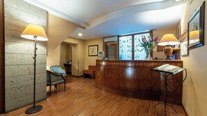 Un área de recepción con un mostrador de madera, dos lámparas de pie, una silla y un ventanal con vidrio decorativo.