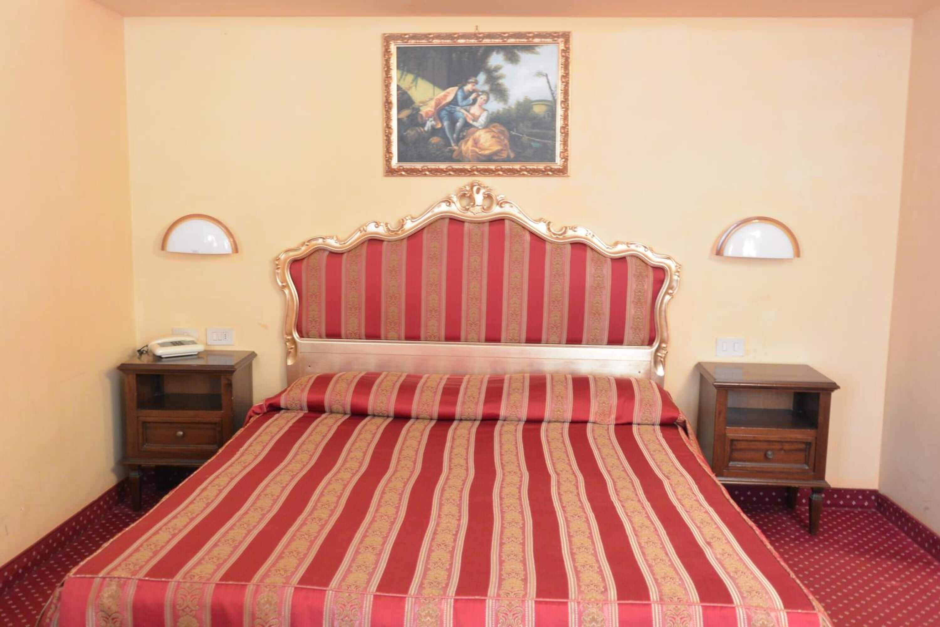 A hotel room with a large bed, two bedside tables, a wall-mounted painting, and two wall sconces.