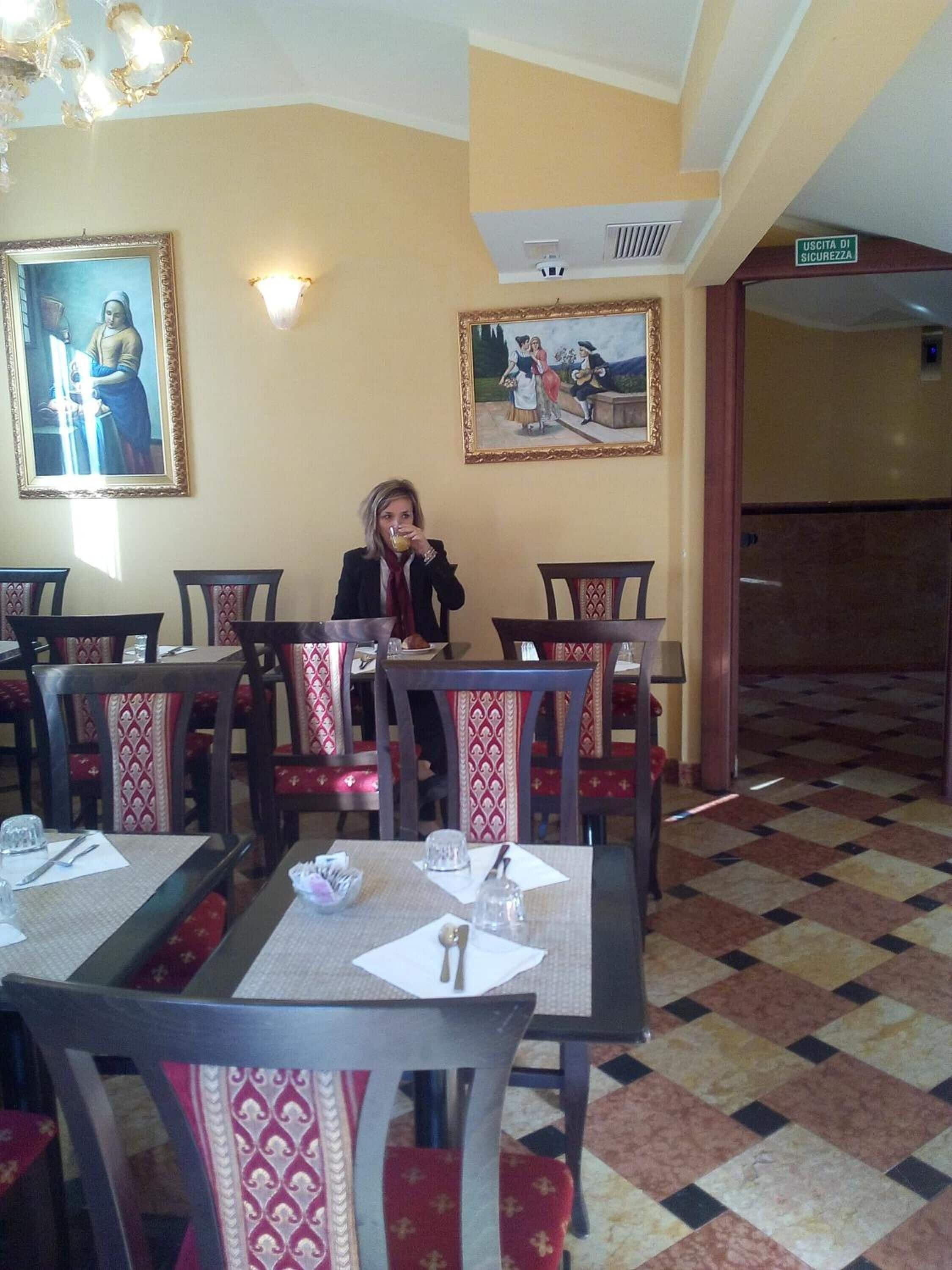 A restaurant interior with tables and chairs, paintings on the walls, and a sign indicating a security exit.