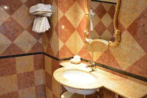 Ein Badezimmer mit Marmorwaschbecken, einem spiegel mit goldener Rahmung und einem Handtuchhalter mit gefalteten Handtüchern.
