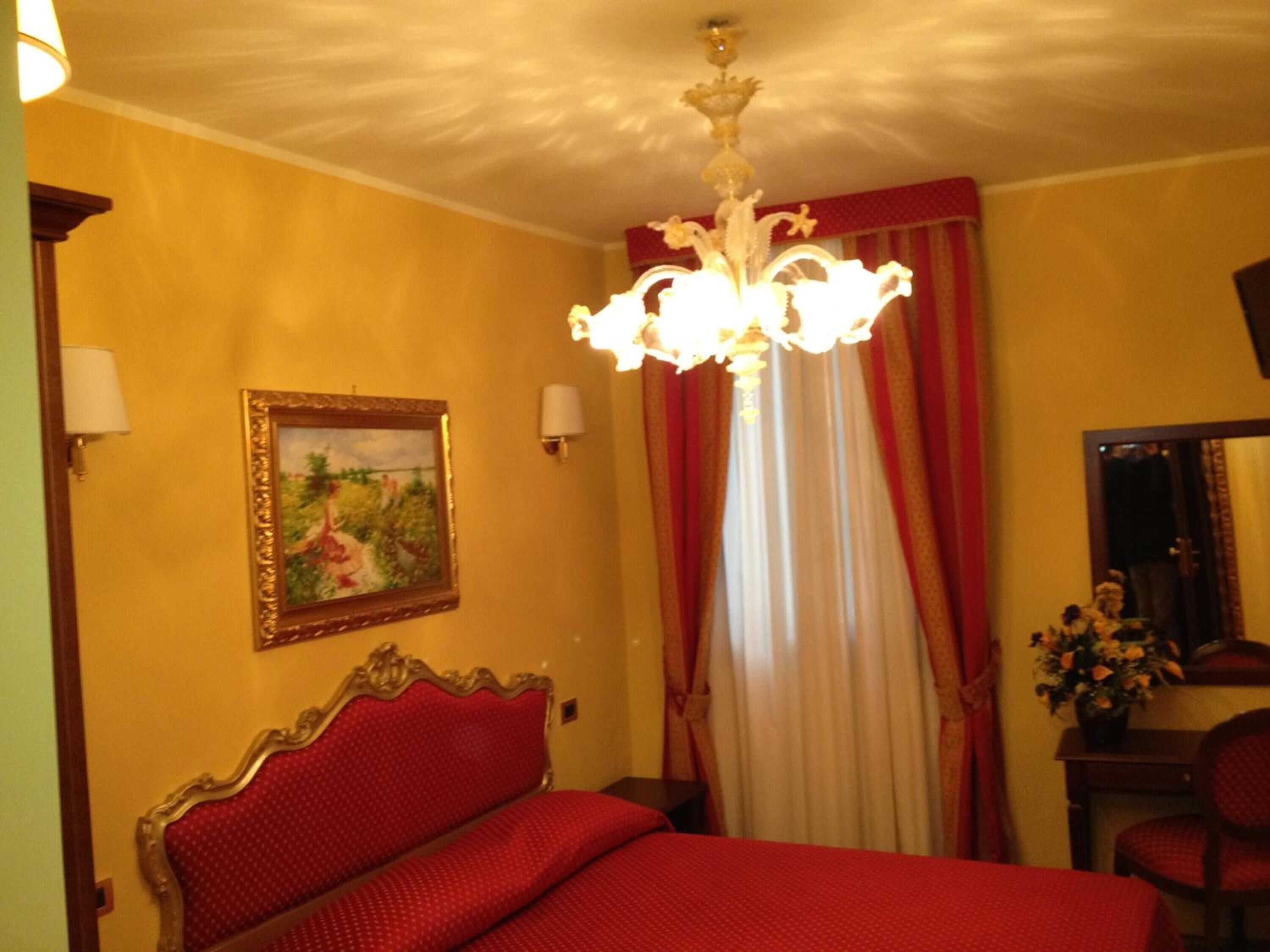 A hotel room with a bed, a chandelier, a painting, and a mirror.
