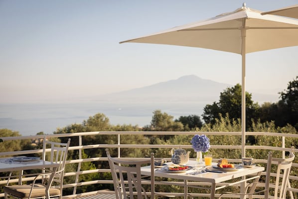 An outdoor dining area with tables and chairs, a table set with plates, a teapot, and a vase of flowers. - Villa Oriana Relais (Sorrento)