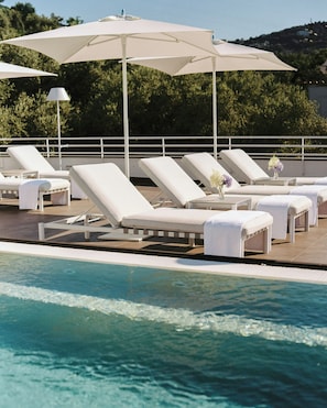 Un área junto a la piscina con sillones de descanso y sombrillas.