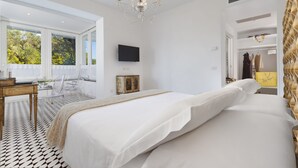 A bedroom with a large bed, a chandelier, a TV, and a window with a view of trees.