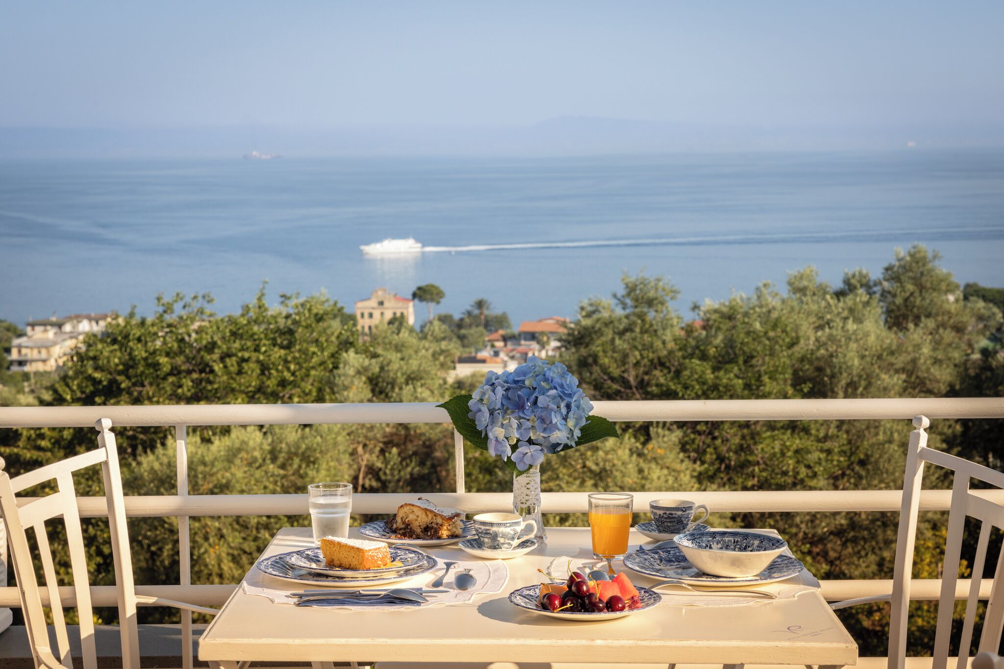 Una mesa preparada con alimentos para el desayuno, un jarrón de flores y vistas al mar.