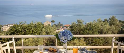 Una mesa preparada con alimentos para el desayuno, un jarrón de flores y vistas al mar.