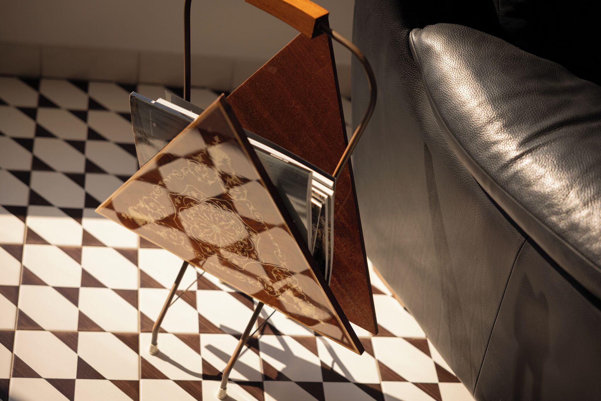 A modern interior with a geometric patterned floor, a leather sofa, and a unique metal and wood side table.