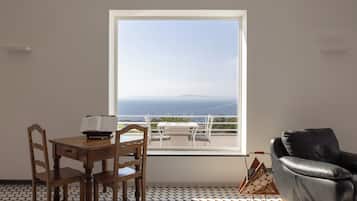 Ein Zimmer mit großem Fenster, einem Esstisch mit Stühlen, einem Ledersofa und einem gemusterten Boden.
