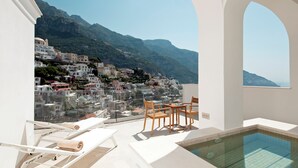 A pool area with a view of a hillside town, lounge chairs, and a small table. - Hotel Posa Posa (Positano)