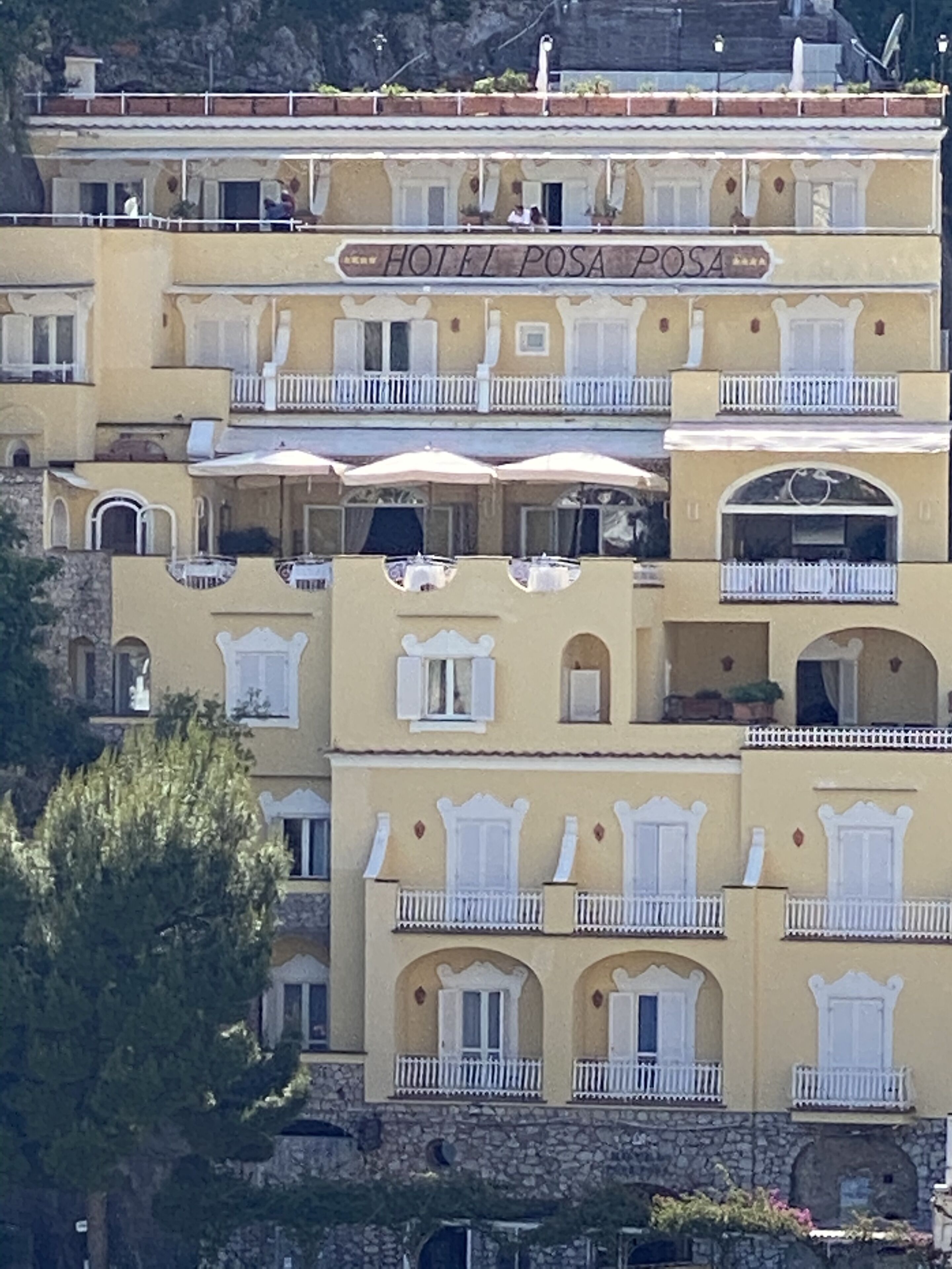 Een meerhoog hotel met balkons, buiten zitplaatsen en een bord met de tekst 'HOTEL POSA POSA'.
