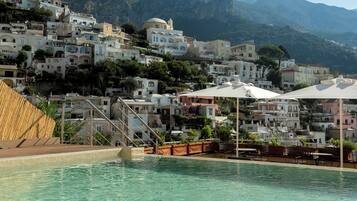 A pool area with clear water, surrounded by buildings with Mediterranean architecture, and mountains in the background.