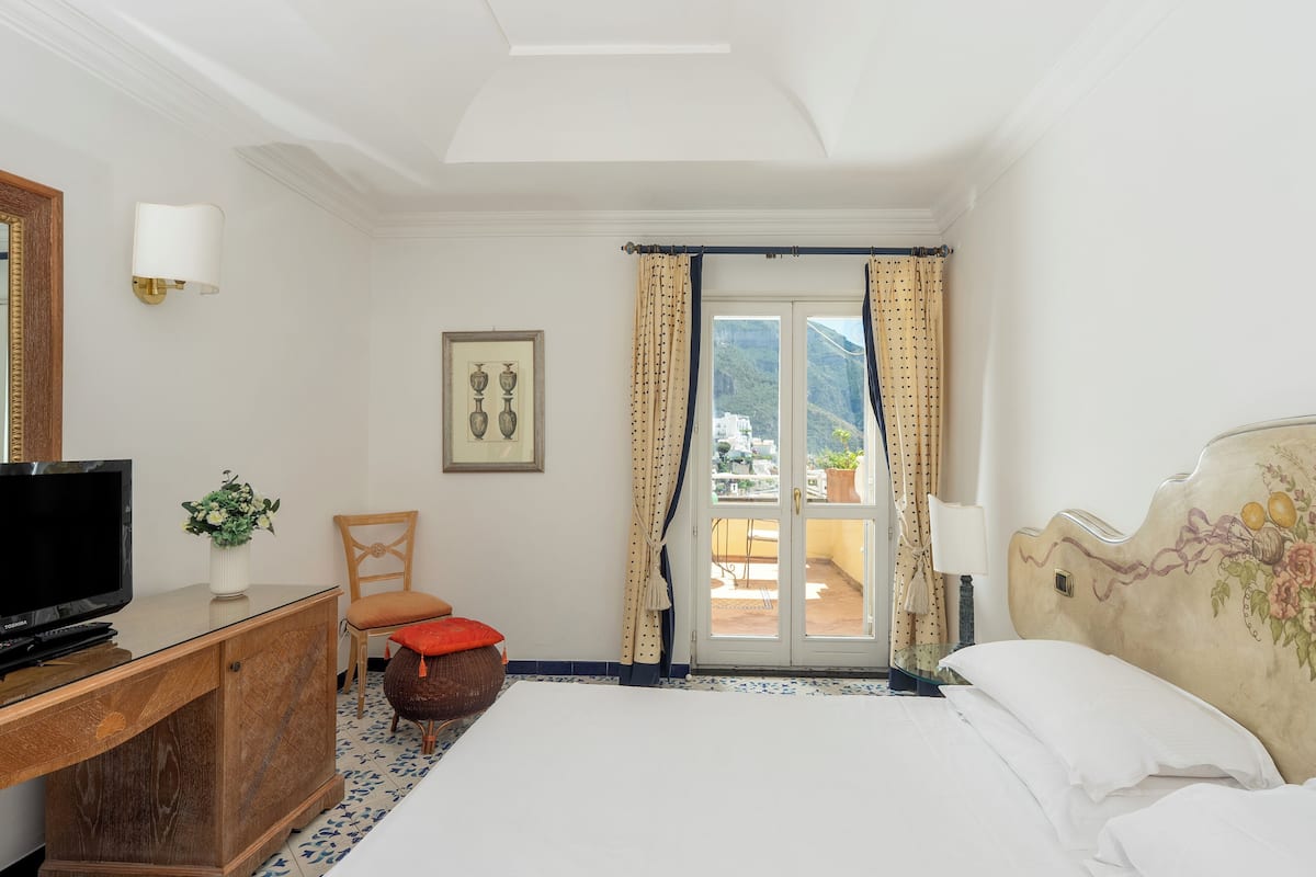 A hotel room with a bed, a television on a wooden cabinet, a chair, and a view of the outdoors through a glass door.